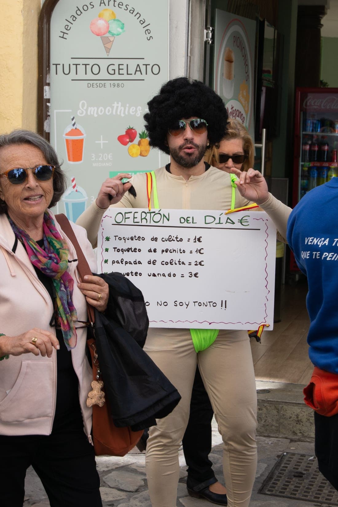 A groom-to-be roams the streets of Granada with his friends in an afro wig holds a hand-lettered specials board outside a Tutto Gelato shop while passers-by wander past